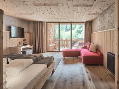 Gemütliches Hotelzimmer mit Holzverkleidung, großem Bett und rotem Sofa mit Blick auf Balkon.