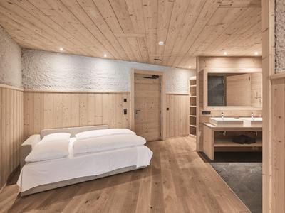 Gemütliches Hotelzimmer mit Holzwänden, Doppelbett und modernem Waschbeckenbereich.