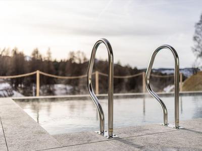 Piscina all'aperto con corrimano in acciaio inox davanti a un paesaggio invernale e cielo nuvoloso.
