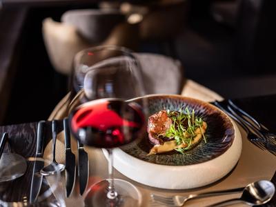 Tavolo di ristorante elegante con un piatto presentato artisticamente e un bicchiere di vino rosso.