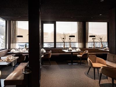 Ristorante d'hotel moderno con illuminazione calda, mobili in legno e pelle, e grandi finestre con vista sul mare.