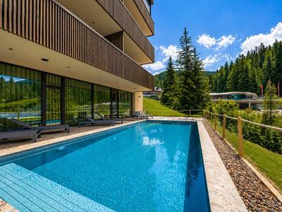 Piscina moderna dell'hotel con acqua azzurra limpida accanto a un edificio a più piani e paesaggio montano verde.