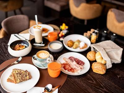 Tavolo con colazione variegata tra cui caffè, pasticcini, pancetta e muesli in un ristorante.
