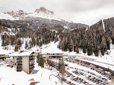 Paesaggio montano invernale con foresta innevata e parcheggio accanto a un hotel.