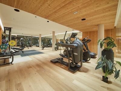 Moderní fitness s dřevěným stropem, běžeckými pásy, závažími a moderním vybavením.