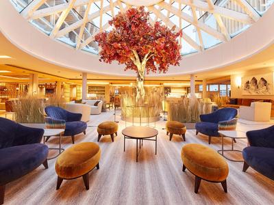 Moderní hotelová lobby s kruhovým skleněným stropem a centrální červenou dekorací stromu.