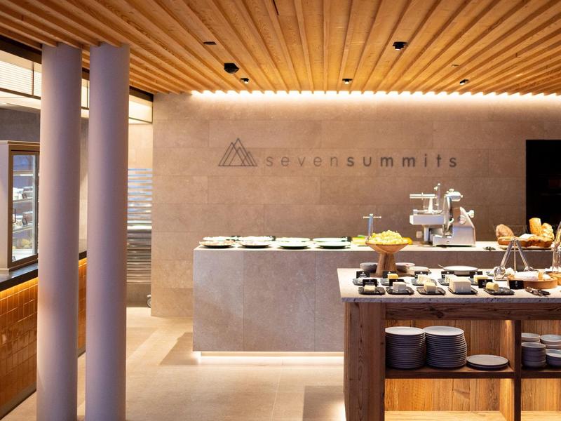 Moderní hotelový bufet s betonem a dřevem, osvětlený teplým stropním světlem.