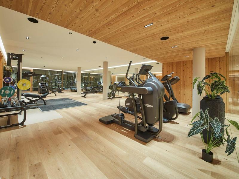 Moderní posilovna se dřevěným stropem, různými cvičebními stroji a velkými zrcadly.