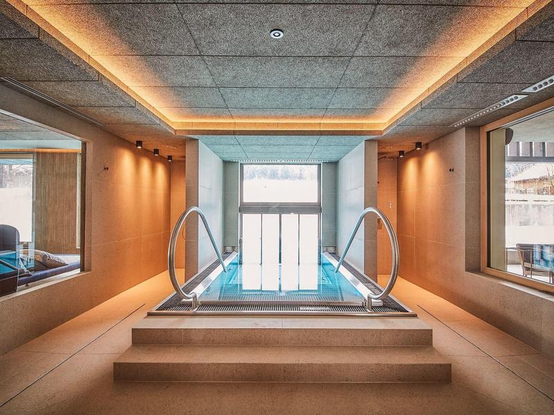 Moderní vnitřní bazén s schodištěm a nepřímým osvětlením v elegantním wellness prostředí.