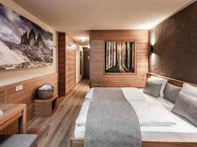 Modern hotel room with large bed, wooden furniture, and landscape paintings on walls.