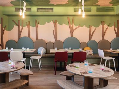 Modern dining area with round wooden tables and upholstered chairs against a green wall with tree design