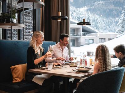 Family sits in a restaurant with panoramic snowy mountain views, enjoying meals together.