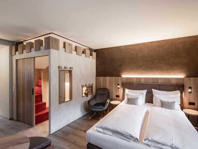 Modern hotel room with two beds, reading chair, and indirect wall lighting.
