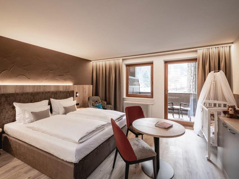 Modern hotel room with large double bed, seating area, and balcony access with mountain view.