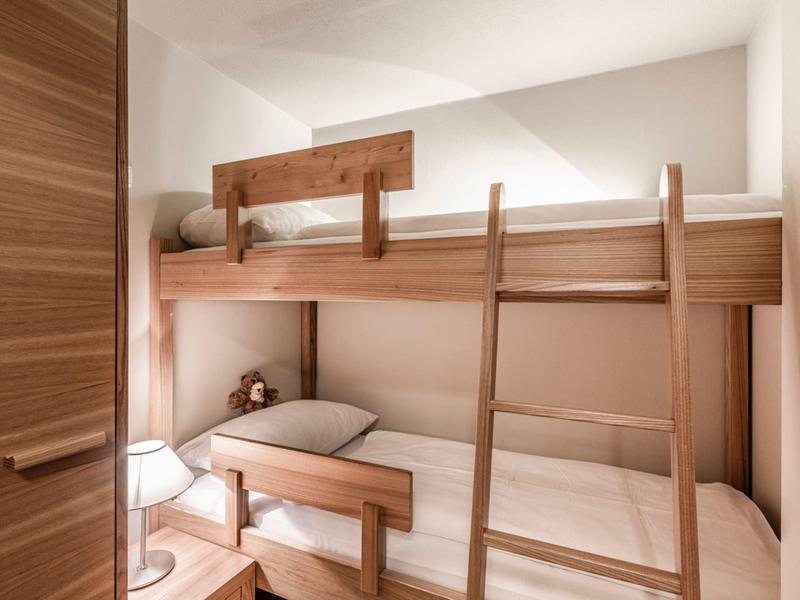Small bedroom with wooden bunk bed and soft lighting.