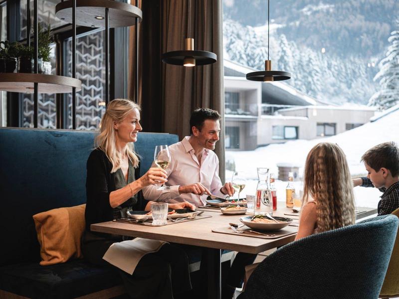 Family sits in a restaurant with panoramic snowy mountain views, enjoying meals together.