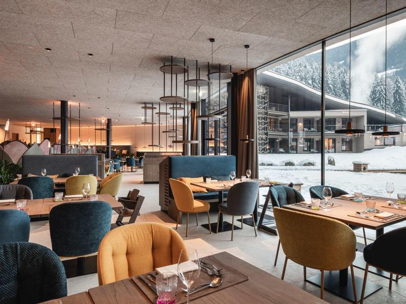 Modern restaurant with colorful chairs and large windows overlooking mountains.