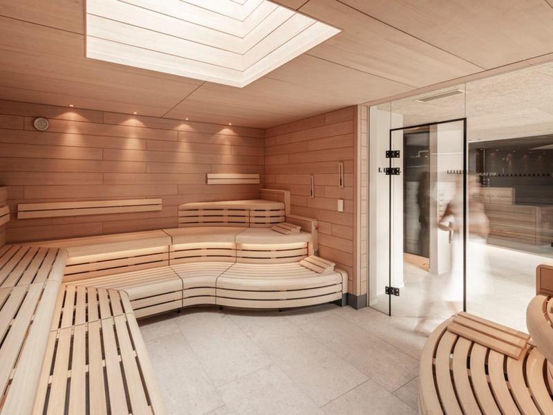 Modern sauna with light wood interior and glass door leading to a pool area.