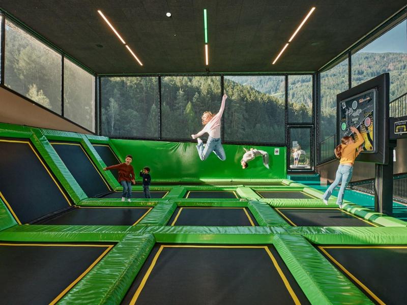 Indoor area with multiple green trampolines and children playing in a hotel recreation zone.