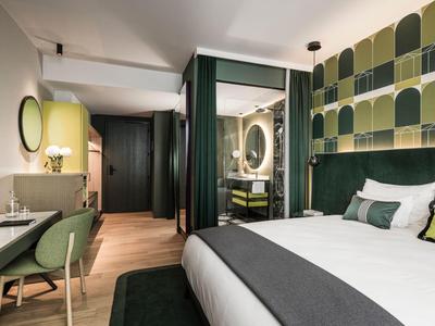 Modernes Hotelzimmer mit Doppelbett, grün-gelben Akzenten und einem Arbeitsplatz mit Stuhl.