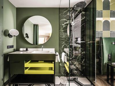 Modernes Hotelbad mit rundem Spiegel und grünem Farbkonzept.