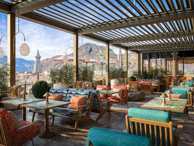 Überdachte Terrasse mit Tischen und Stühlen, dekoriert mit Pflanzen und Kissen, mit Bergblick.