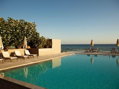Una piscina tranquilla dell'hotel con lettini e vista sul mare sotto un cielo sereno.
