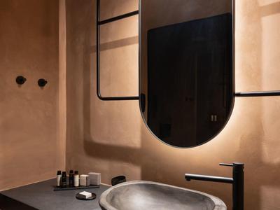 Modern bathroom with oval mirror, concrete sink, black faucet, and warm beige walls.
