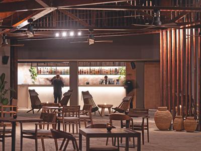 Area bar con mobili in legno e due persone al bancone illuminato in un hotel.