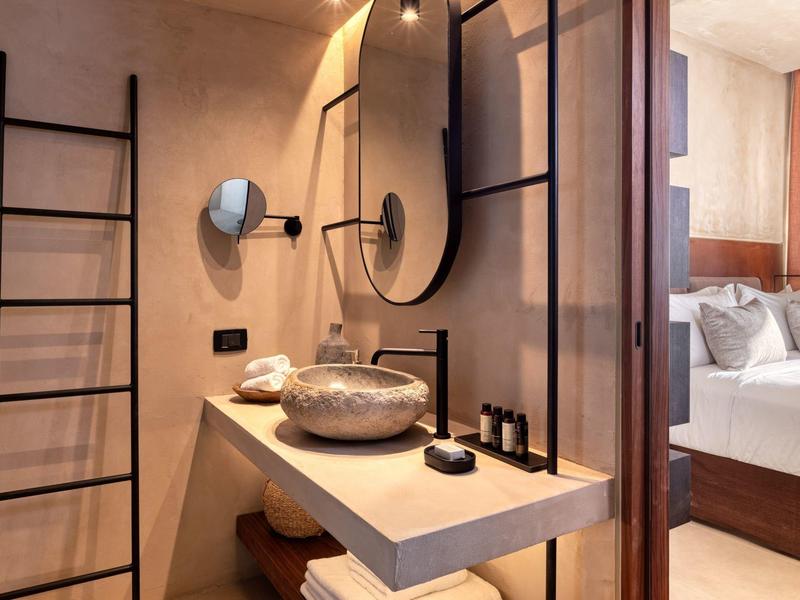 Modern bathroom with stone sink, black fixtures, ladder towel rack, and view into bedroom