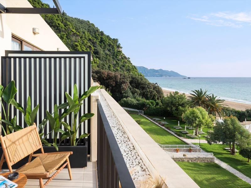Balcony with chair overlooking green garden and blue sea under clear sky