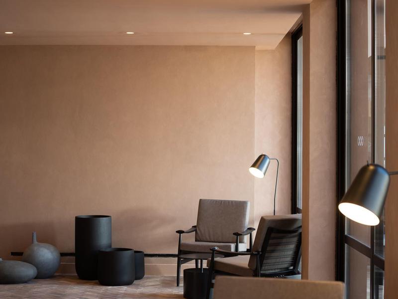 Área de descanso moderna con sillones negros, lámpara de mesa y grandes ventanas en una habitación de hotel.