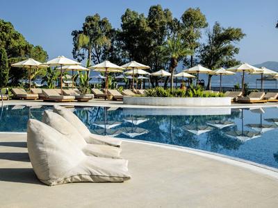 Poolbereich eines Hotels mit Liegestühlen, Sonnenschirmen und umgeben von Bäumen bei klarem Himmel