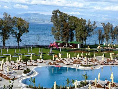 Piscina al aire libre con sombrillas y tumbonas junto a un lago y árboles al fondo.