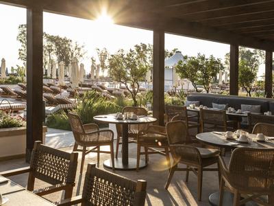 Lounge al aire libre bañada por el sol con mesas y sillas junto a una piscina en un hotel.