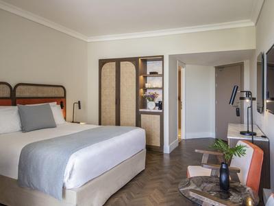 Habitación de hotel moderna con cama grande, armario y zona de estar en luz cálida.