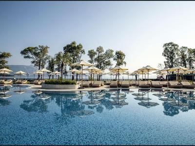 Großer Hotelpool mit Sonnenschirmen und Bäumen an einem sonnigen Tag