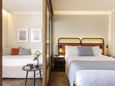 Habitación de hotel moderna con cama doble, armario con espejo y zona de estar acogedora en tonos neutros.