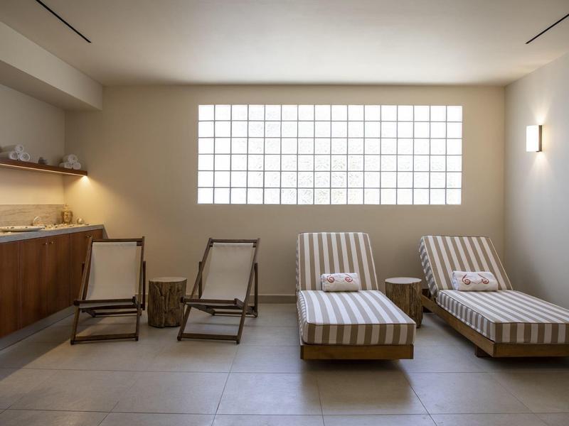 Sala de descanso moderna con dos tumbonas y dos sillas junto a una ventana grande.