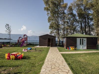Parco giochi per bambini con altalene, scivolo e casette nel giardino verde vicino all'acqua.