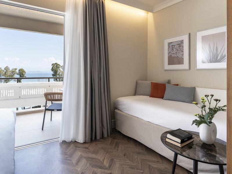 Lounge dell'hotel luminosa con letto da giorno, tavolino e balcone con vista sul mare.