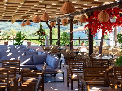 Offener Sitzbereich eines Restaurants mit Holztischen und blauen Sofas unter einem überdachten Dach.