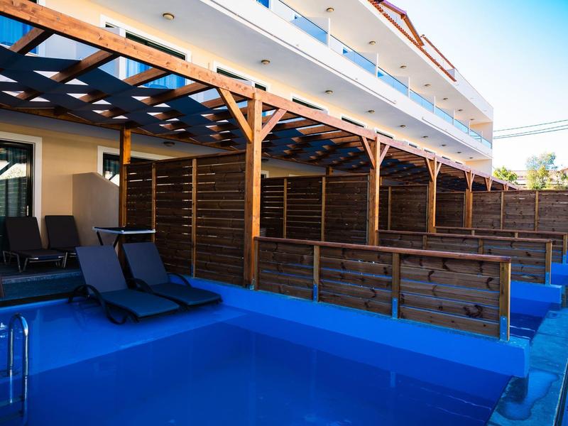 Schwimmbereich mit blauem Pool, zwei Liegestühlen und hölzernem Sonnenschutz an einem Hotel.