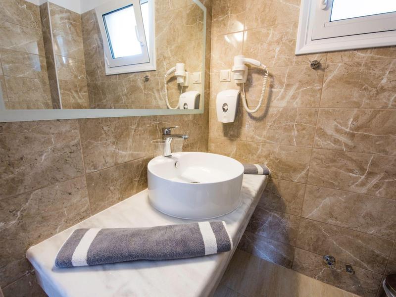 Kleines Badezimmer mit rundem Waschbecken, Handtuch und Marmorfliesen an den Wänden.