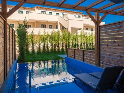 Privater Pool auf einer Terrasse mit Blick auf eine moderne Hotelanlage bei Sonnenschein.