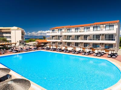 Velký venkovní bazén před třípatrovou budovou hotelu pod jasně modrou oblohou.