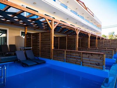 Piscina esterna blu con lettini sotto una pergola di legno, edificio sullo sfondo.