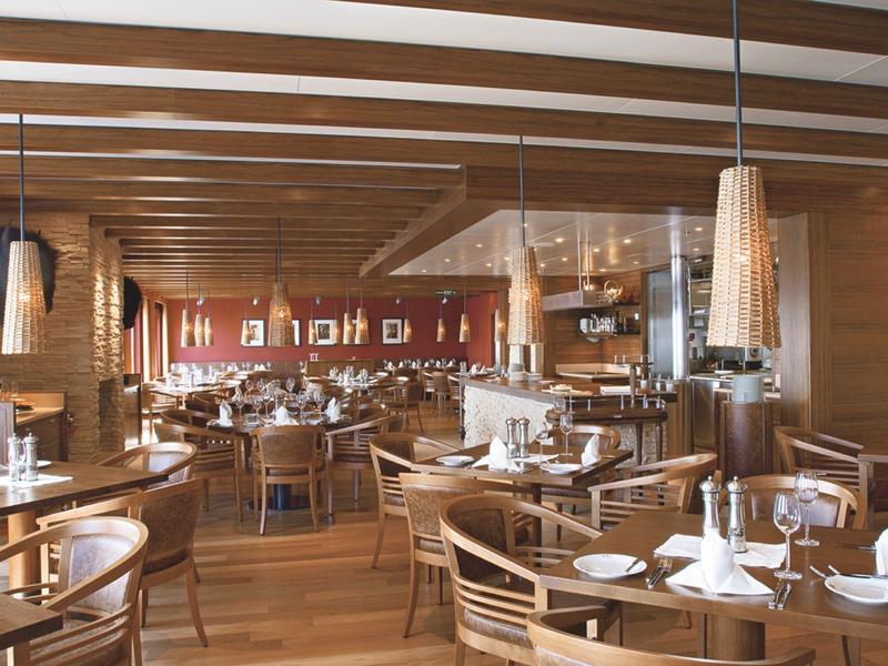 Sala da pranzo luminosa con legno chiaro, tavoli apparecchiati e lampade moderne.