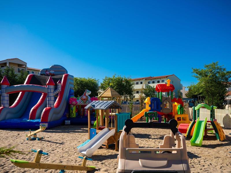 Area giochi colorata con scivoli e altalene su terreno sabbioso.