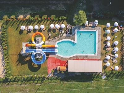 Aerial view of a pool with water slides and sun umbrellas surrounded by greenery.